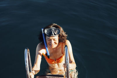 High angle view of happy woman climbing ladder of boat on sea