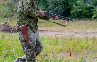 Unknown man in camouflage clothing walks with a rifle while shooting off bullets