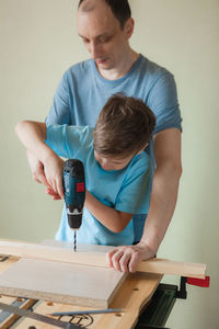 Dad and son work together while standing at workbench. little boy learning to drill. 