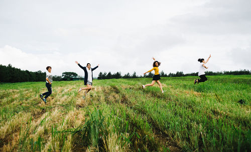 Full length of female friends jumping over agricultural field against sky