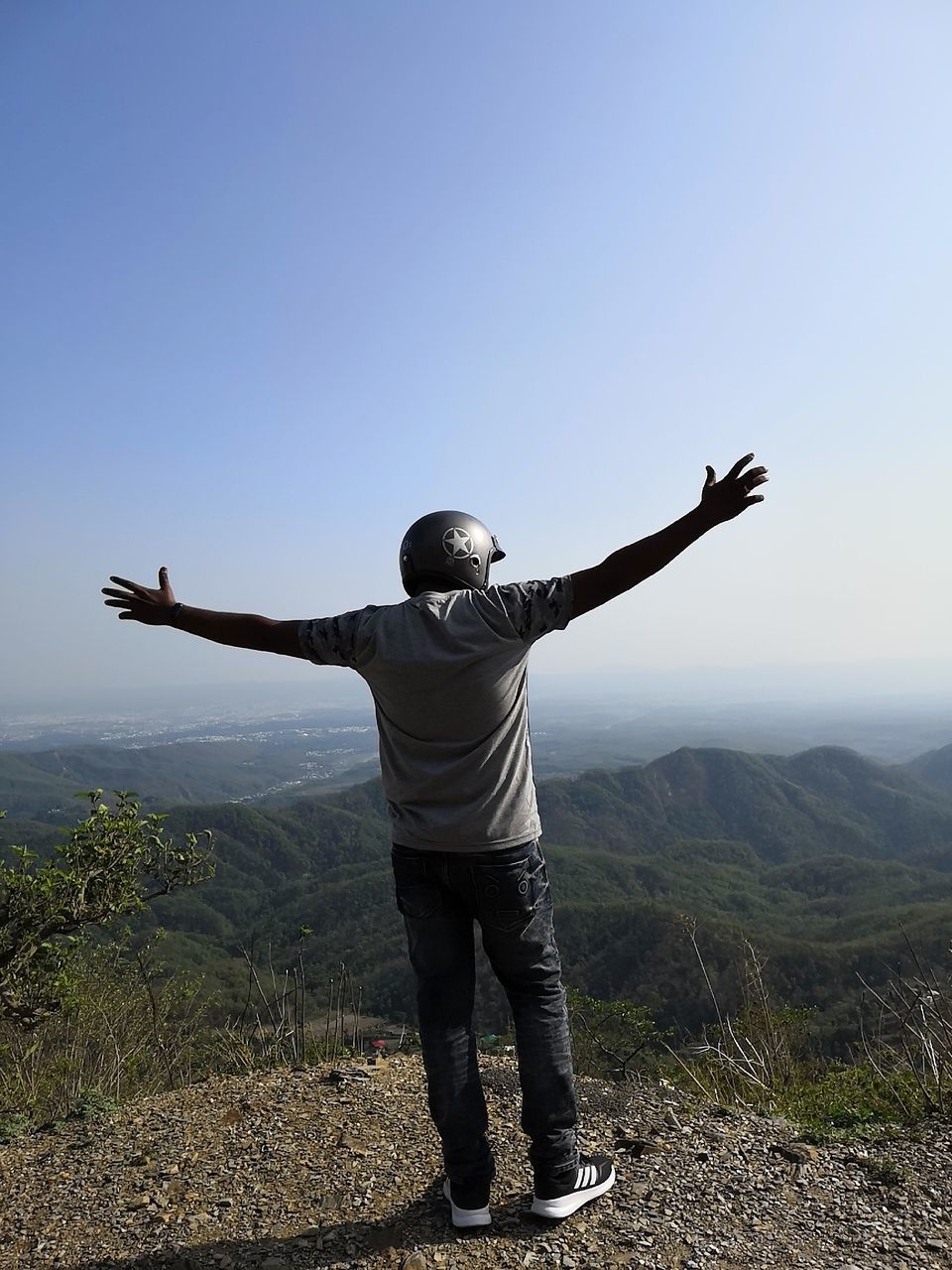 REAR VIEW OF MAN WITH ARMS RAISED STANDING AGAINST SKY