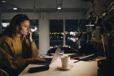 Side view of dedicated mature businesswoman using laptop while working late at creative office