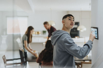 Teenage boy adjusting lights of room through digital tablet mounted on wall by family