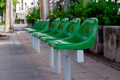 Empty chairs and tables by sidewalk against trees