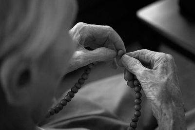 Cropped image of senior woman praying rosary beads at home