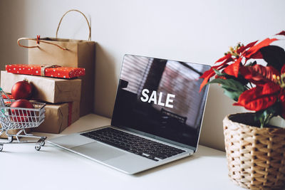 Open laptop computer with word sale on display screen, poinsettias christmas flower and gift boxes