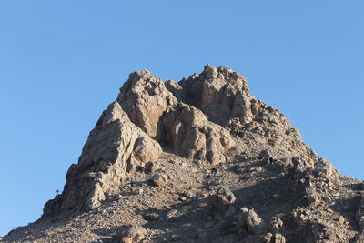 Low angle view of cliff against clear blue sky