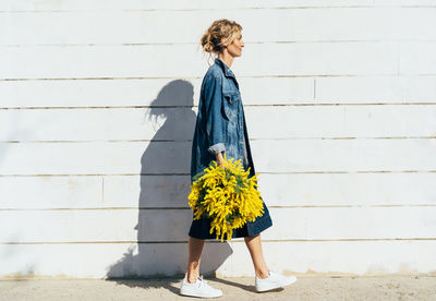 Woman standing by flower against wall