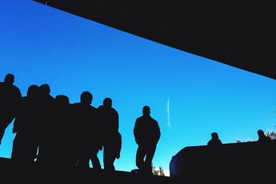 Low angle view of silhouette people against blue sky