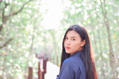 Portrait of young woman standing against trees