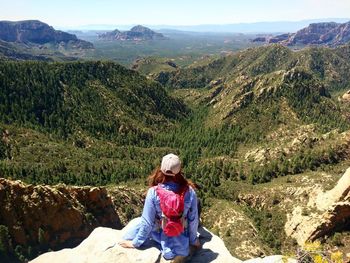 Rear view of woman sitting on rock against mountains