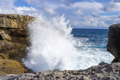 Waves splashing on rocks at shore against sky