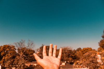 Cropped hand gesturing against clear blue sky