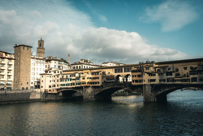 Bridge over river by buildings in city against sky