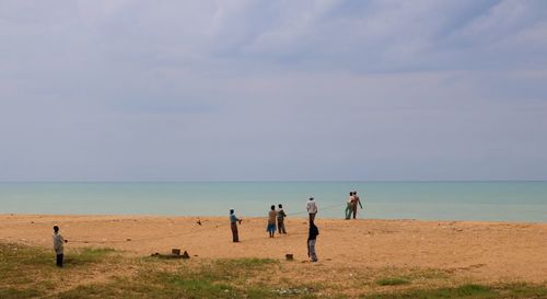 People pulling rope on beach against sky