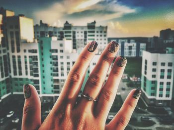 Cropped hand showing nail polish in front of city at sunset