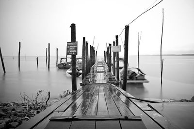 Sailboats moored on pier by sea against sky