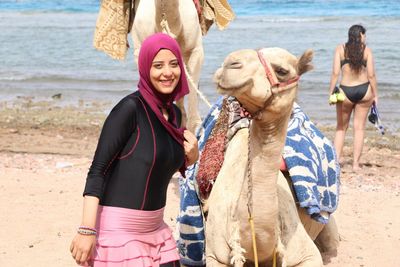 Portrait of smiling woman standing by camel at beach