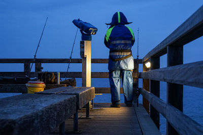 Rear view of man standing on pier against sky
