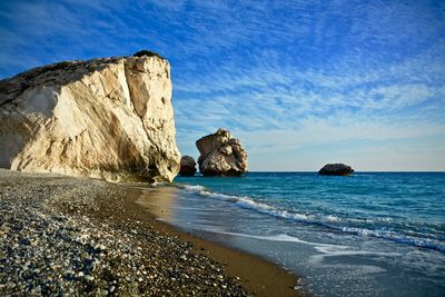 Low angle view of rock formation by sea against cloudy blue sky on sunny day