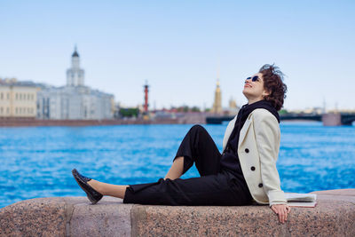 Caucasian happy girl sits on granite curb city with book. in a white coat