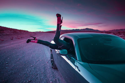 Low section of woman peeking from car window on road against sky