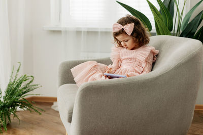 A little girl is sitting in a chair playing a game on her phone or watching cartoons