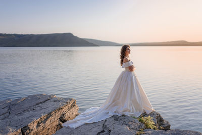 Rear view of woman sitting on rock by sea against sky