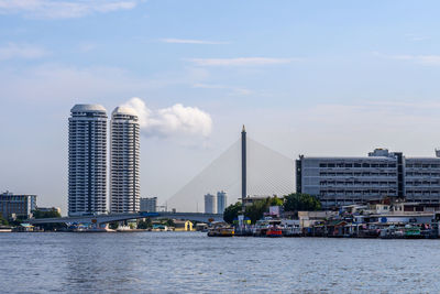 Modern buildings by river against sky in city