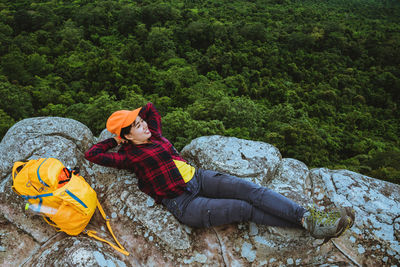 High angle view of female hiker lying on cliff against forest