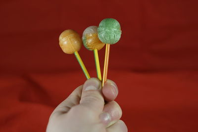 Cropped hand holding lollipop against red fabric