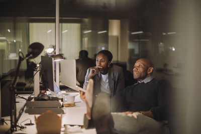 Ambitious male and female colleagues discussing over laptop in office at night