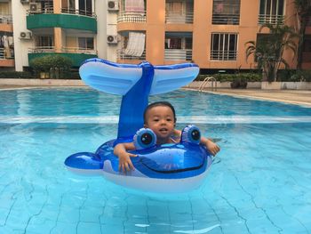 Portrait of cute baby girl with inflatable ring in swimming pool against buildings