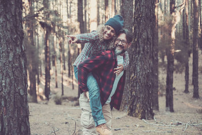Smiling man carrying woman on back against tree