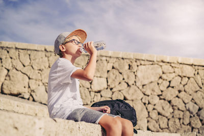 Rear view of boy holding umbrella against stone wall