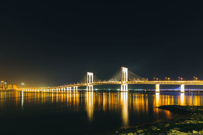 Illuminated bridge over river against sky at night