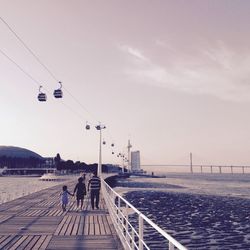 Family on promenade with overhead cable cars against sky