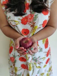 Midsection of woman holding red while standing against white wall