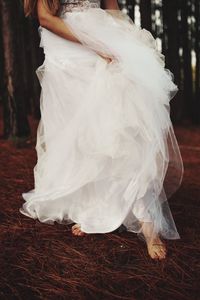 Low section of bride wearing wedding dress while standing on field