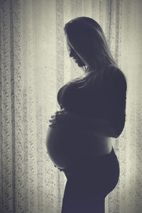 Side view of young woman standing against curtain