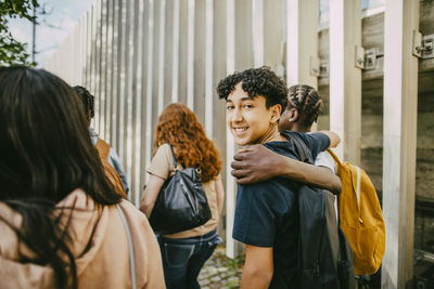 Portrait of smiling teenage boy walking with arm around friend near fence