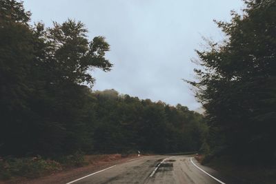 Empty country road along trees and against clear sky