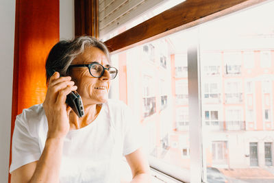 Mature woman talking on phone by window