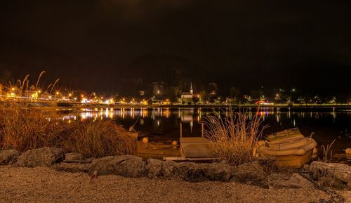 Illuminated city by river against sky at night