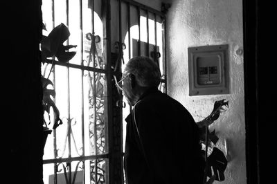 Rear view of man standing by window at home