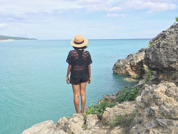 Rear view of woman standing on rock by sea