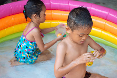 Siblings holding toys in wading pool