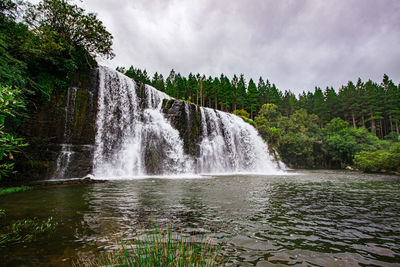 Scenic view of waterfall in forest against sky