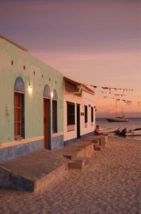 Building on beach against sky during sunset