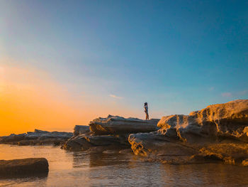 Yung asian women standing on rock by sea against sky during sunset